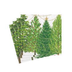 three napkins with christmas trees on them and lights strung from the trees in the background