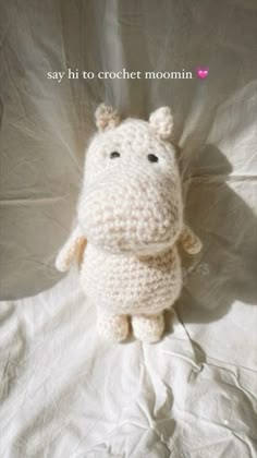 a crocheted hippo laying on top of a white sheet with the caption say hi to crochet moomin