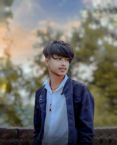 a young man standing in front of a tree filled sky with his hands on his hips