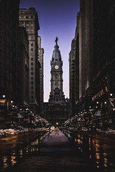 a large clock tower towering over a city street at night with lights reflecting in the water