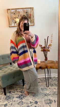 a woman taking a selfie in front of a mirror with her cell phone and colorful sweater