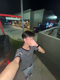 a young man covering his eyes while standing next to a car