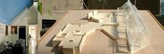 a wooden model of a house on top of a table next to a building with windows and doors