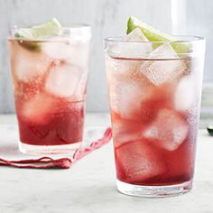 two glasses filled with ice and limes on top of a white marble countertop