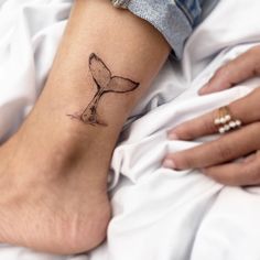 a woman's foot with a whale tail tattoo on her left ankle and hand