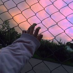 someone is reaching up to the sky through a chain link fence with their hand on it