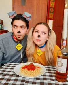 a man and woman sitting at a table with spaghetti in front of their faces,