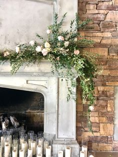 candles are lined up in front of a fireplace with flowers and greenery on it