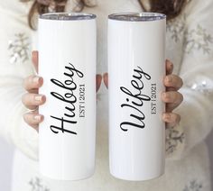 two women holding white coffee mugs with black lettering