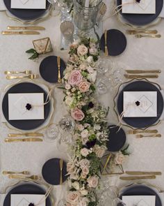 the table is set with black and white plates, silverware, and floral centerpieces