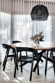 a dining room table with black chairs and a flower arrangement on the table in front of sheer curtains