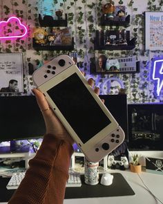 a person holding up a nintendo wii game controller in front of a wall with pictures on it