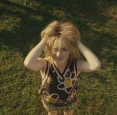 a woman standing in the grass holding her hair up to her head with both hands