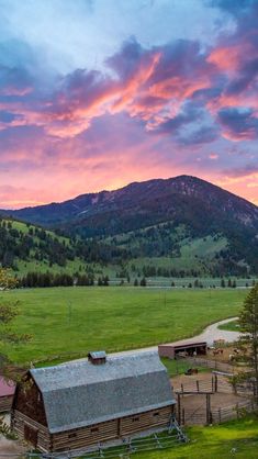 an old barn sits in the middle of a green field with mountains in the background