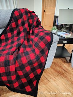 a red and black plaid blanket sitting on top of a couch next to a table