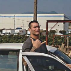 a man standing next to a white car giving the peace sign with his right hand