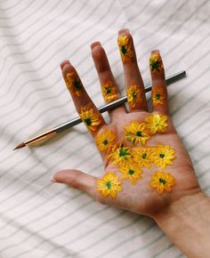 someones hand with yellow flowers painted on it and a pen in the other hand