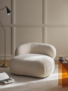 a white chair sitting on top of a wooden floor next to a lamp and table