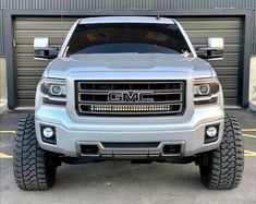 the front end of a silver truck parked in a parking lot next to garage doors