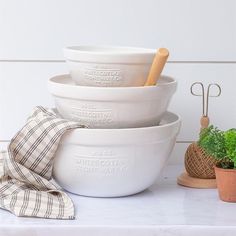 three white bowls stacked on top of each other next to a potted green plant