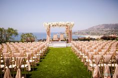 an outdoor ceremony set up with chairs and flowers on the aisle, overlooking the ocean