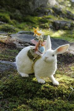 a white bunny with a flower crown on its head sitting in the mossy ground