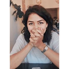 a woman sitting at a table with her hands folded in front of her face