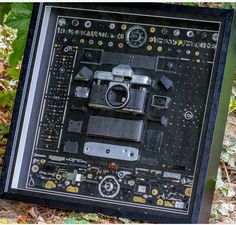 an old camera sitting on top of a piece of metal in front of some leaves