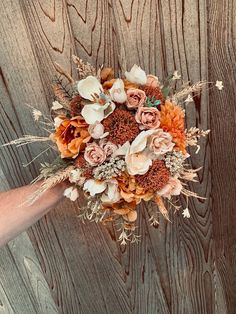 a person holding a bouquet of flowers on top of a wooden table next to a wall