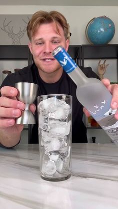 a man is holding a bottle in front of a glass filled with ice cubes