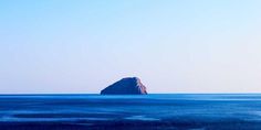 an island in the middle of the ocean with blue sky and water around it on a sunny day