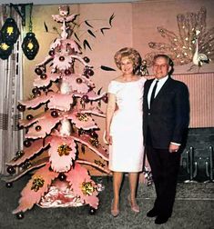 a man and woman standing next to a pink christmas tree