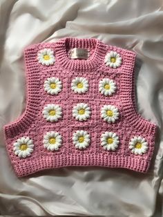 a pink knitted sweater with white and yellow flowers on the front, sitting on a bed