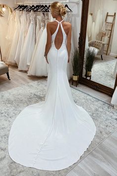 a woman standing in front of a mirror wearing a white wedding dress with an open back