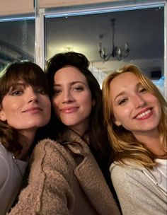 three women are posing for the camera in front of a window with their arms around each other