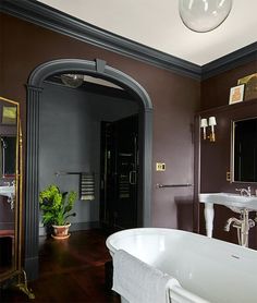 a bath tub sitting next to a white sink under a bathroom mirror on top of a wooden floor