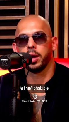 a bald man wearing sunglasses talking into a microphone