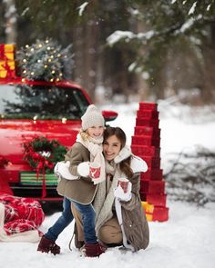 two girls in the snow next to a red truck and christmas tree with lights on it