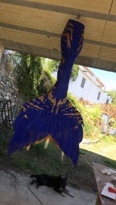 a black cat laying under a blue and yellow bird decoration on a wooden porch with a house in the background