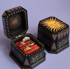 two decorative boxes with rings in them on a purple surface, one is open and the other is closed