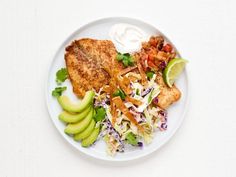 a white plate topped with fish, coleslaw and avocado next to sour cream