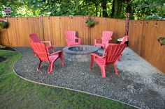 a fire pit surrounded by red chairs in a back yard with a wooden fence behind it