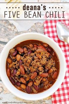 a white bowl filled with beans and meat on top of a red checkered table cloth