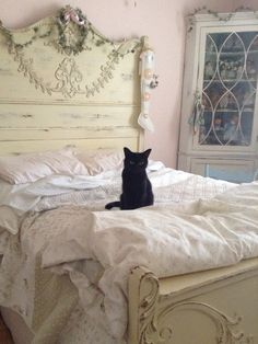 a black cat sitting on top of a white bed in a room with pink walls