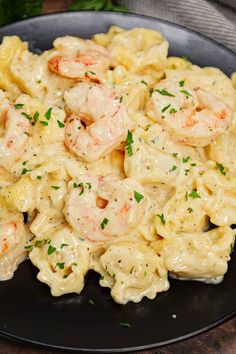 pasta with shrimp and cream sauce on a black plate, garnished with parsley