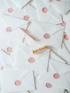 some white envelopes with pink wax stamping and a pen on top of them