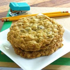 two cookies sitting on top of a white plate next to pencils and paper clips