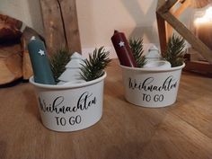 two white ceramic cups with christmas decorations in them sitting on a table next to a candle