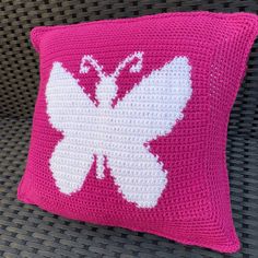 a crocheted butterfly pillow on a wicker chair with pink and white trim