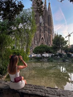 a woman sitting on a wall looking at the water in front of a building under construction